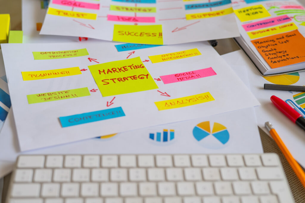 Marketing strategy planning sheet with colorful sticky notes, charts, and a keyboard on a desk.